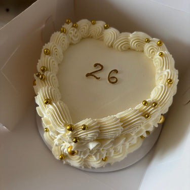 A cream heart cake with pearls, a cream border and the gold inscription '26'
