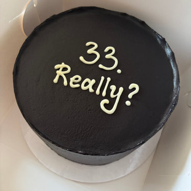 Кръгла черна торта с надпис '33. Really?' в бял текст, без допълнителна украса.