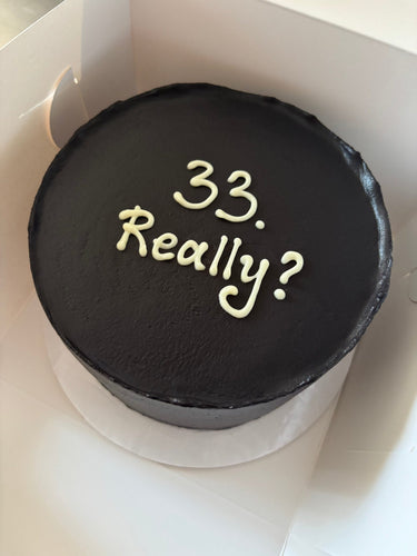 Кръгла черна торта с надпис '33. Really?' в бял текст, без допълнителна украса.