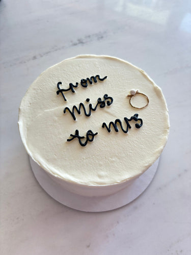 Кръгла бяла торта, декорирана с перли и надпис 'from Miss to Mrs'