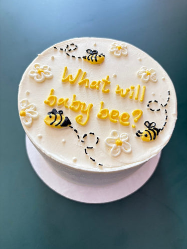 Кръгла бяла торта с рисунка и надпис 'What will baby bee?' за разкриване на пола на бебето.
