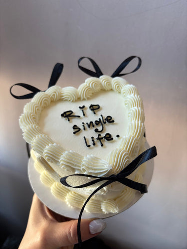 Кремава торта сърце с надпис RIP single life, украсена с панделки и кремав кант.