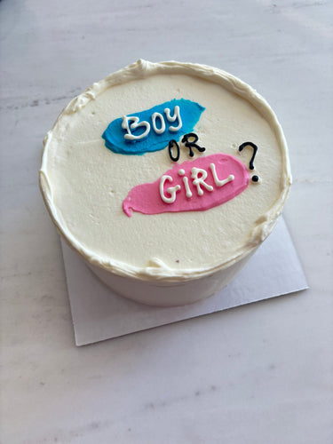 Кръгла бяла торта с надпис Boy or Girl? върху горната повърхност, без допълнителна украса.