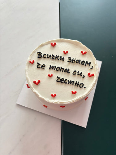 Кръгла бяла торта с надпис "Всички знаем, че топа си, честно." и декоративни сърца.