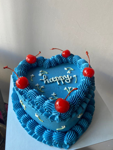 Синя торта с форма на сърце, украсена с черешки и кремав кант, с надпис "happy"