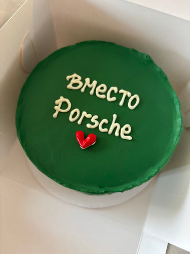 Кръгла зелена торта с надпис "Вместо Porsche" в бял или контрастен цвят отгоре.