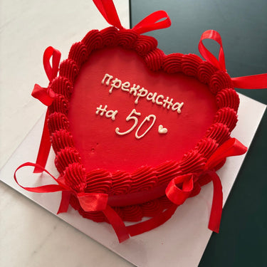 Round red cake with the message "gorgeous at 50", a cream border and decorative ribbons.