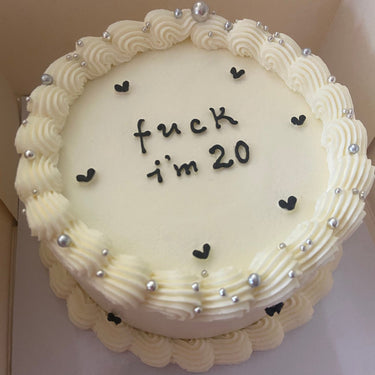 Кръгла кремава торта с надпис 'fuck i'm 20', украсена с перлени декорации и кремав кант.