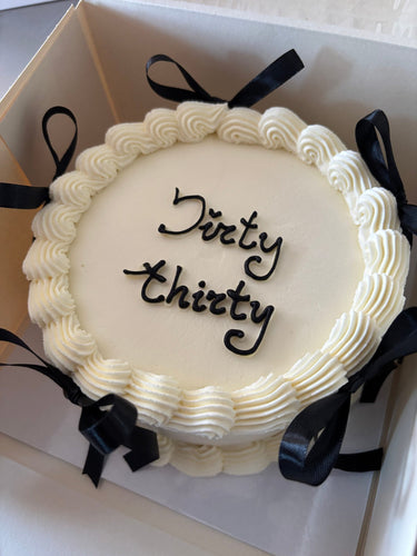 Кръгла бяла торта с надпис "Dirty thirty", украсена с панделки и кремав кант