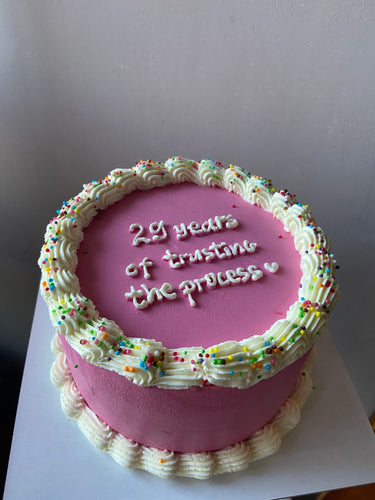 Кръгла розова торта с кремав кант и надпис 29 years of trusting the process ♡