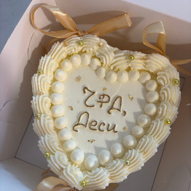 White heart-shaped cake with gold pearls, ribbons and gold lettering Happy Birthday, Desi.