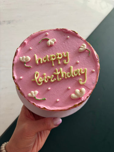 Кръгла розова торта с надпис happy birthday, украсена с бели перли.