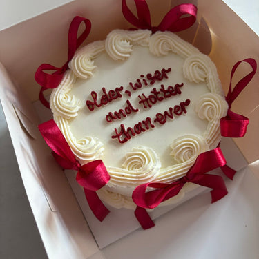 Round white cake with a cream border and ribbons, with the message 'older, wiser and hotter than ever'