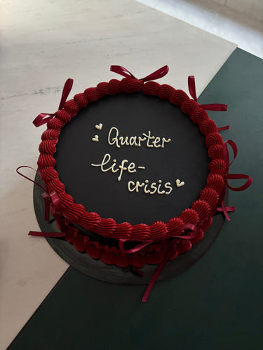Кръгла черна торта с кремав кант и панделки, надпис 'Quarter life-crisis'