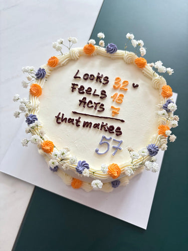 Кръгла кремава торта с кремав кант и надпис "Looks 32 ♥ Feels 18 Acts 7 that makes 57"