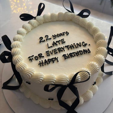 Кръгла бяла торта с кремав кант и панделки, надпис '22 years LATE FOR EVERYTHING. Happy BIRTHDAY'