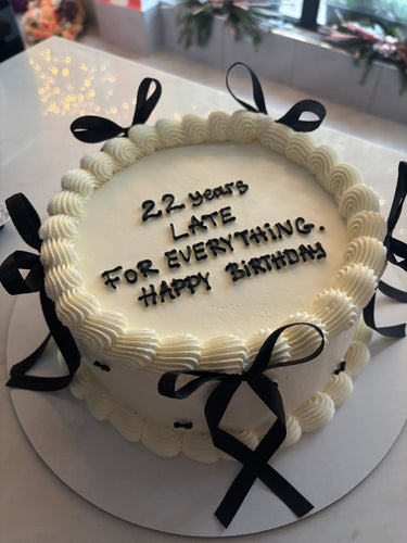 Кръгла бяла торта с кремав кант и панделки, надпис '22 years LATE FOR EVERYTHING. Happy BIRTHDAY'