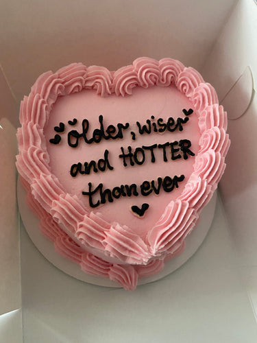 Розова торта сърце с кремав кант и надпис 'older, wiser and HOTTER than ever'