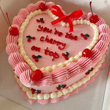 Розова торта сърце с кремав кант, панделки и черешки, надпис you're the cherry on top.