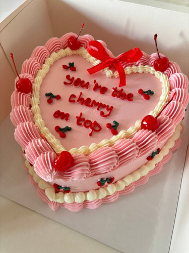 Розова торта сърце с кремав кант, панделки и черешки, надпис you're the cherry on top.