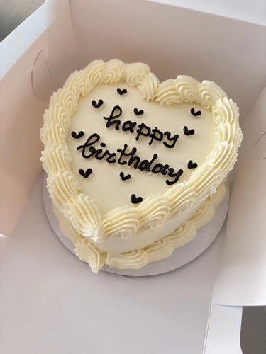 Кремава торта във форма на сърце с кремав кант и надпис 'happy birthday'.