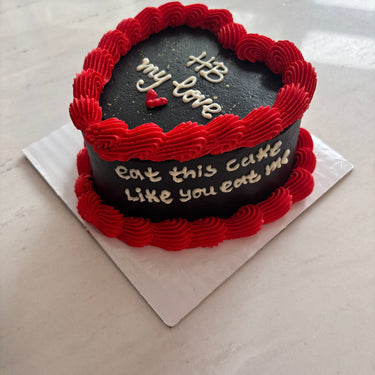 Черна торта сърце с кремав кант по ръба и страничен надпис 'HB my love / eat this cake like you eat me'.