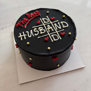 Кръгла черна торта с надпис The Best HUSBAND, украсена с рисунка и декоративни перли.