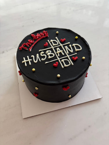 Кръгла черна торта с надпис The Best HUSBAND, украсена с рисунка и декоративни перли.