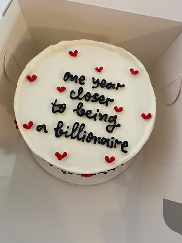 Кръгла бяла торта с надпис 'one year closer to being a billionaire'
