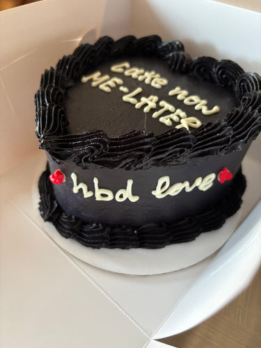 Черна торта във форма на сърце с кремав кант и страничен надпис 'cake now ME-LATER hbd love'