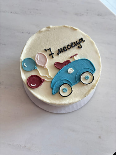 Кръгла бяла торта с рисунка на кола и балони за бебешка месечинка.