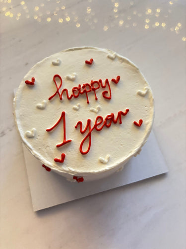 Кръгла бяла торта с надпис 'happy 1 year' за годишнина, без допълнителна украса