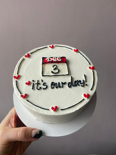 Кръгла бяла торта с рисунка, кремав кант и надпис 'Dec 3 it's our day!' за годишнина