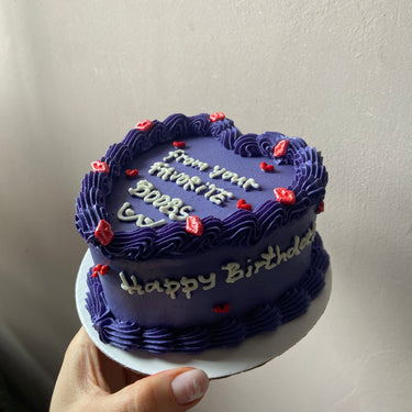 Лилава торта с форма на сърце, кремав кант и страничен надпис 'Happy Birthday' за рожден ден