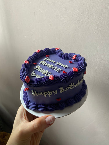 Лилава торта с форма на сърце, кремав кант и страничен надпис 'Happy Birthday' за рожден ден