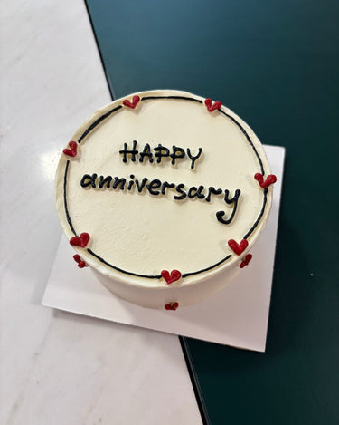 Кръгла бяла торта за годишнина с рисунка на сърца, кремав кант и надпис HAPPY Anniversary