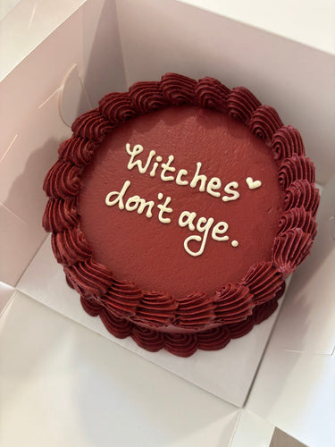 Кръгла бордо торта с кремав кант и надпис 'Witches don't age.'