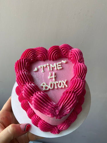 Розова торта с форма на сърце с брокат и кремав кант, надпис 'TIME 4 BOTOX' върху повърхността.