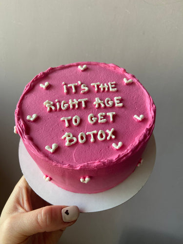 Кръгла розова торта с надпис 'IT'S THE RIGHT AGE TO GET BOTOX' отгоре, без допълнителна украса.