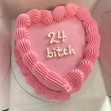 Heart-shaped cake with pink icing, a cream border and the inscription '24 bitch' on top.