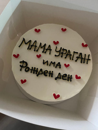 Кръгла бяла торта с надпис 'МАМА УРАГАН има Рожден ден' отгоре, без допълнителна украса.