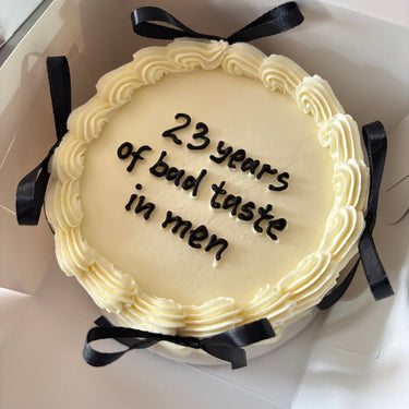Кремава кръгла торта с панделки, кремав кант и надпис '23 years of bad taste in men'