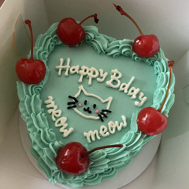 Сърцевидна ментова торта с рисунка на коте, черешки, кремав кант и надпис 'Happy Bday meow meow meow'.
