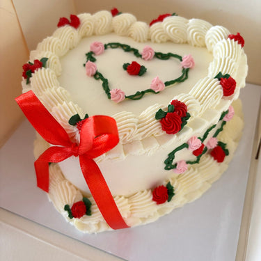 Heart-shaped cake, cream icing, decorated with ribbons and a cream border, no message