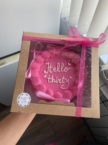 Кръгла розова торта с надпис Hello thirty, декорирана с панделки, кремав кант и брокат.
