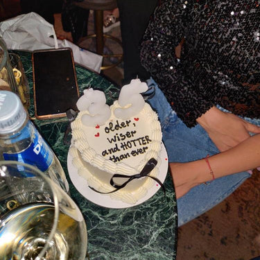 White heart-shaped cake with ribbons, a cream border and the inscription 'older, wiser and HOTTER than ever'.