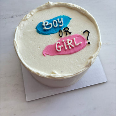 Кръгла бяла торта с надпис Boy or Girl? върху горната повърхност, без допълнителна украса.