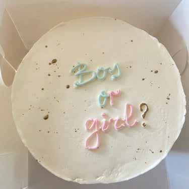 Кръгла бяла торта с надпис 'Boy or girl?' в златни букви.