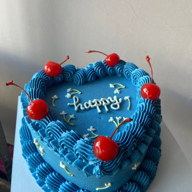 Синя торта с форма на сърце, украсена с черешки и кремав кант, с надпис "happy"