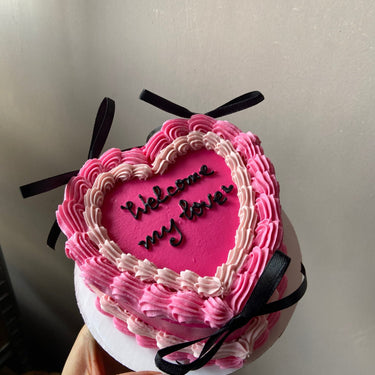 Розова торта във форма на сърце с надпис Welcome my love, кремав кант и декоративни панделки.